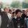 Nelson Mandela, an older black man with graying hair, forms a raised fist with his right hand and holds it above his head. With his left, he is holding hands with Winnie Mandela, a black woman with dark hair. She is smiling and has formed a raised fist with her left hand, mirroring Nelson Mandela’s raised fist. A large crowd is gathered behind them.